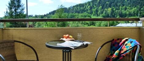 A balcony with wicker chairs, a small round table with a fruit bowl, a glass, and a book.