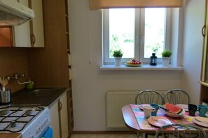 A kitchen with a stove, sink, and window with plants. There is a table with chairs and a plate of food.