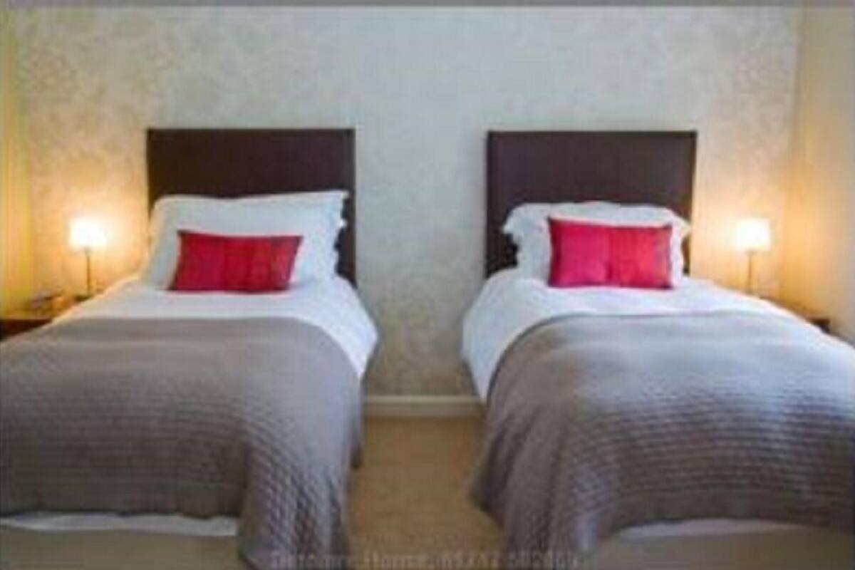 Habitación de hotel con dos camas, cada una con cabecera, ropa de cama blanca y almohada roja decorativa.