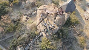 An aerial view of a rural area with thatched-roof houses, a stone staircase leading to a viewing platform, and a clear path. - Stephen Margolis Resort (Harare)