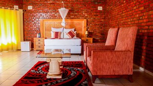 A room with a brick wall, a wooden bed, a red sofa, a coffee table, and a patterned rug. - Stephen Margolis Resort (Harare)