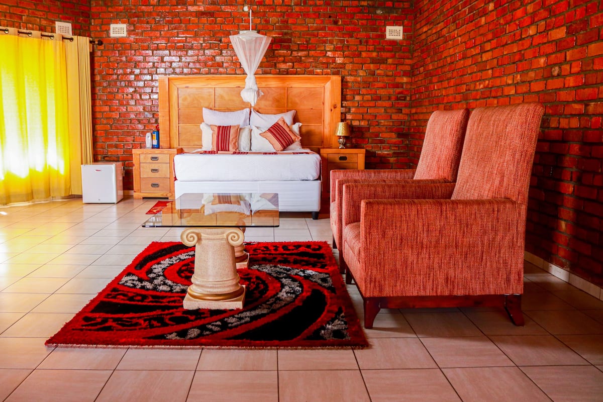 Ein Zimmer mit Backsteinwand, einem hölzernen Bett, einem roten Sofa, einem Couchtisch und einem gemusterten Teppich.