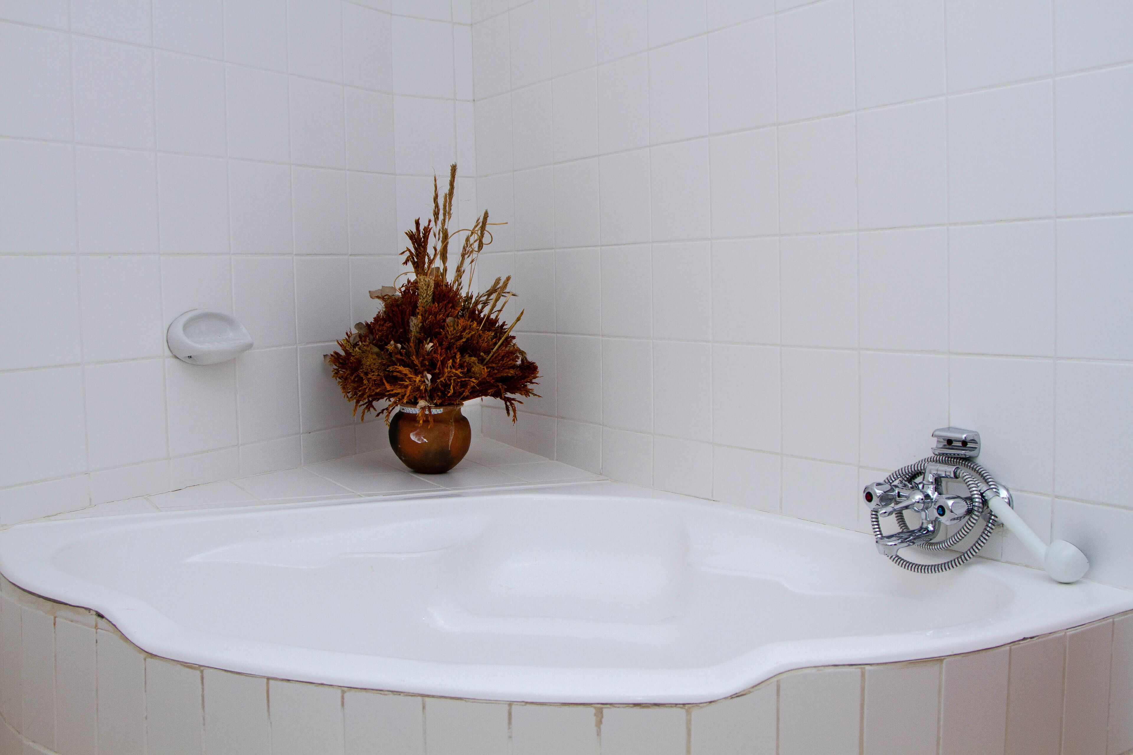 A bathroom with a white bathtub, a brown vase with dried plants, and a handheld showerhead.