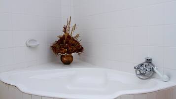 A bathroom with a white bathtub, a brown vase with dried plants, and a handheld showerhead.