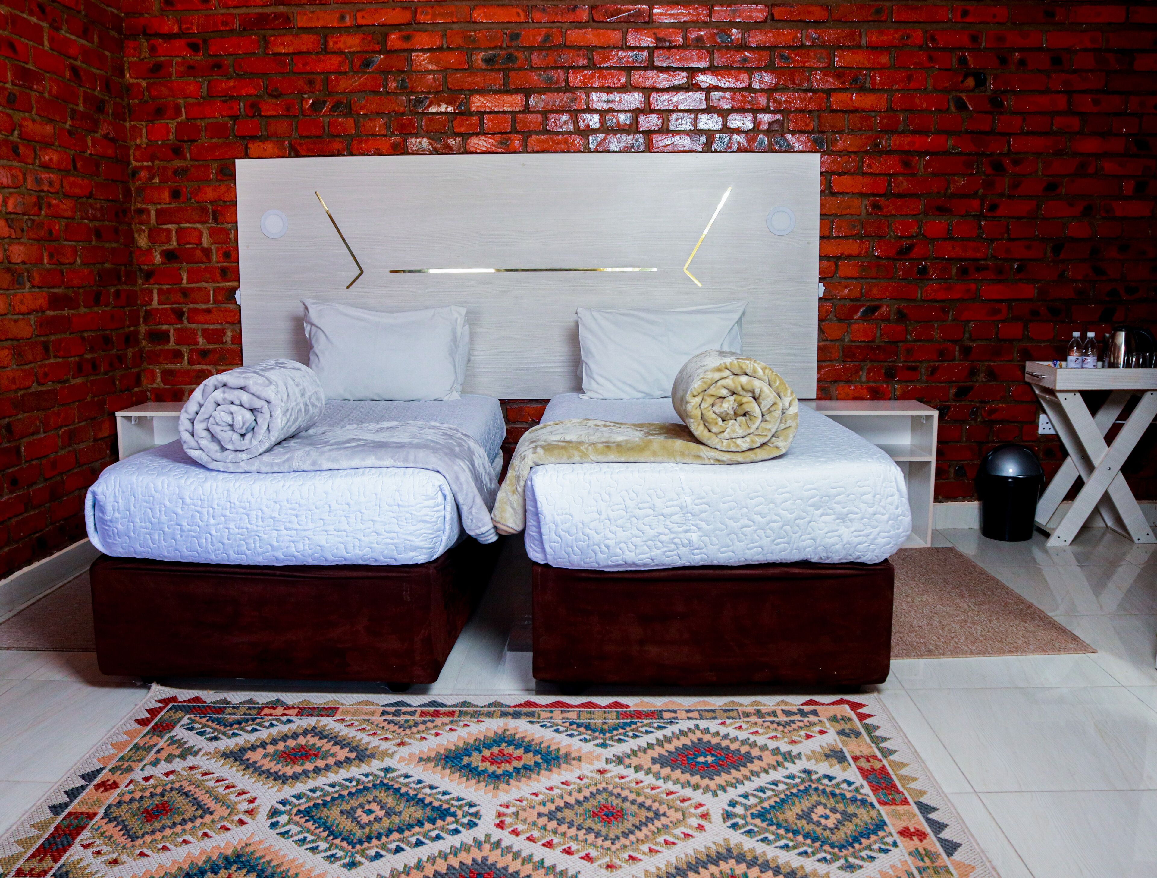 Une chambre avec deux lits, un mur en briques et un tapis à motifs.