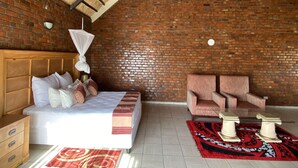 A bedroom with a brick wall, a sloped ceiling, a bed with pillows, a chair, and a table. - Stephen Margolis Resort (Harare)