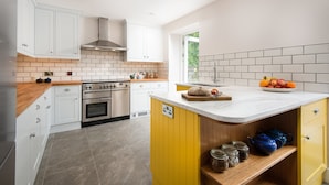 A modern kitchen with white cabinets, a central island with a sink, and a yellow accent wall. - Mill House (Crieff)