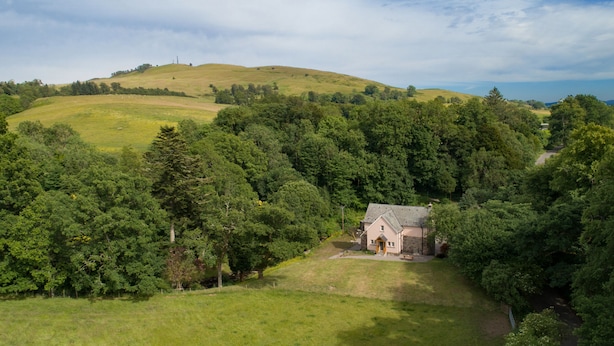 A rural house surrounded by dense forest, with a hill in the background. - Mill House (Crieff)