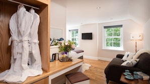 A modern hotel room with a wooden desk, a seating area with a sofa, a TV mounted on the wall, and a window with a view of greenery. - Mill House (Crieff)