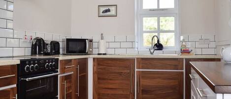 A kitchen with wooden cabinets, a stove, a microwave, and a window.