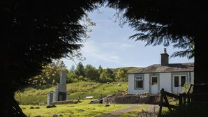A white house with a stone chimney, a stone structure, and a grassy area with sheep. - Brae Cottage (Crieff)