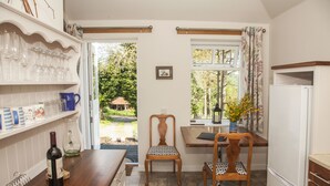 A kitchen with a wooden table, chairs, a wine bottle, and a refrigerator. - Brae Cottage (Crieff)