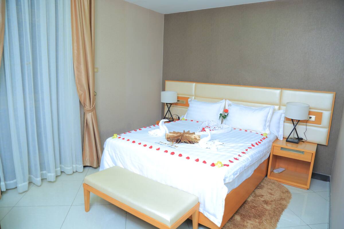 A neatly made bed with a white bedspread, two bedside lamps, a wooden nightstand, and a bench at the foot of the bed.