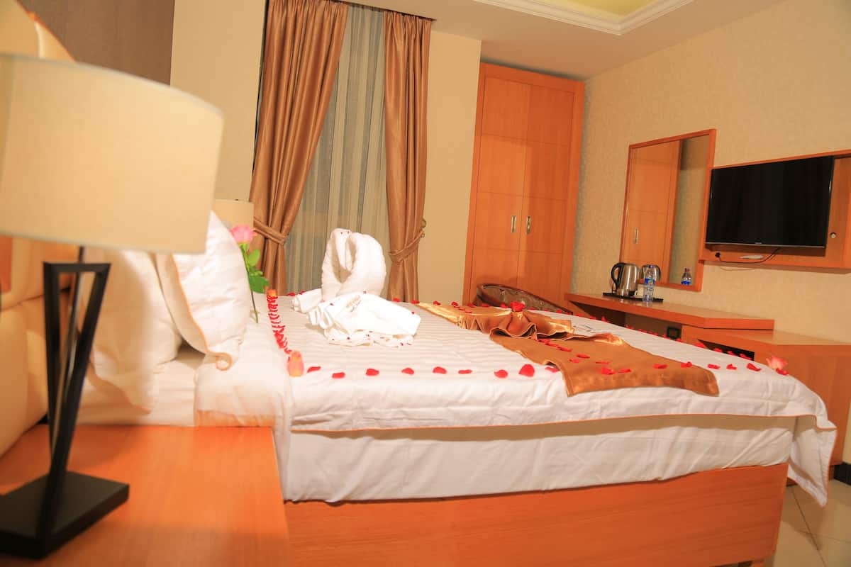 A hotel room with a neatly made bed, a wooden nightstand, a television, and a mirror on the wall.