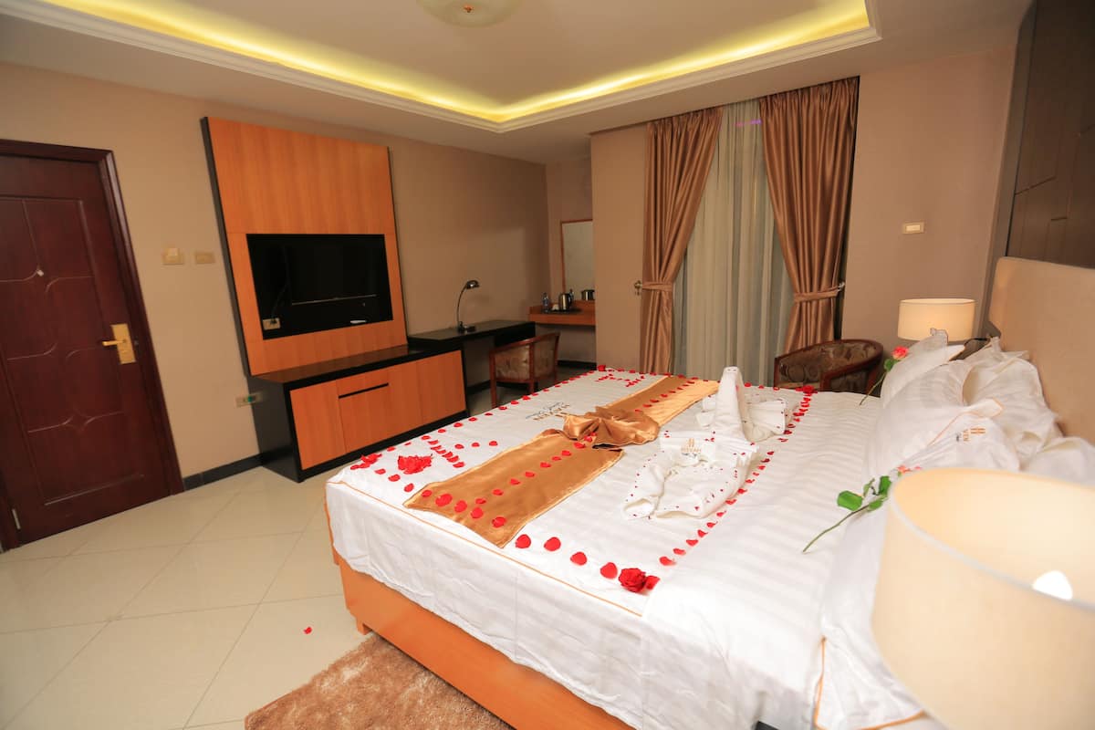 A hotel room with a large bed, a TV mounted on the wall, a desk with a chair, and a bathroom visible through an open door.