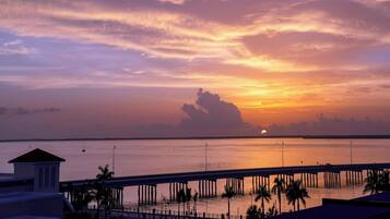 Atardecer sobre una superficie acuática tranquila con un puente y palmeras al frente.