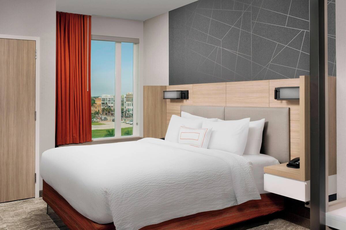A modern hotel room with a large bed, a view of the city, and a wooden headboard.
