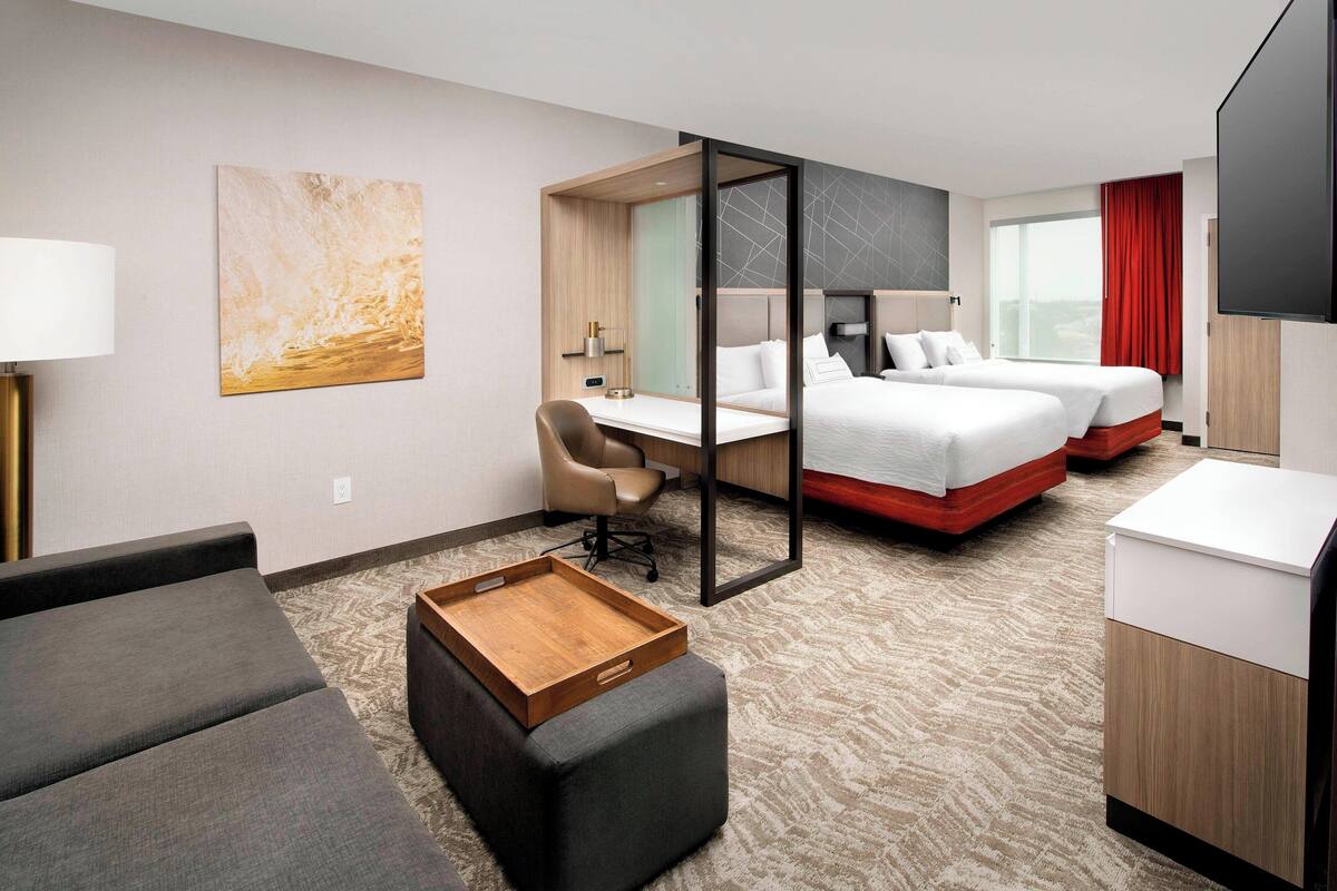 A hotel room with a bed, a desk, a chair, a TV, and a window with curtains.