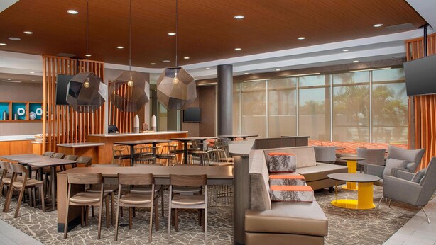 A modern hotel lobby with wooden furniture, a central bar area, and large windows offering a view of palm trees. - SpringHill Suites by Marriott Punta Gorda Harborside (Punta Gorda)