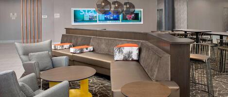 A modern hotel lobby with a sectional sofa, round tables, and a bar area.