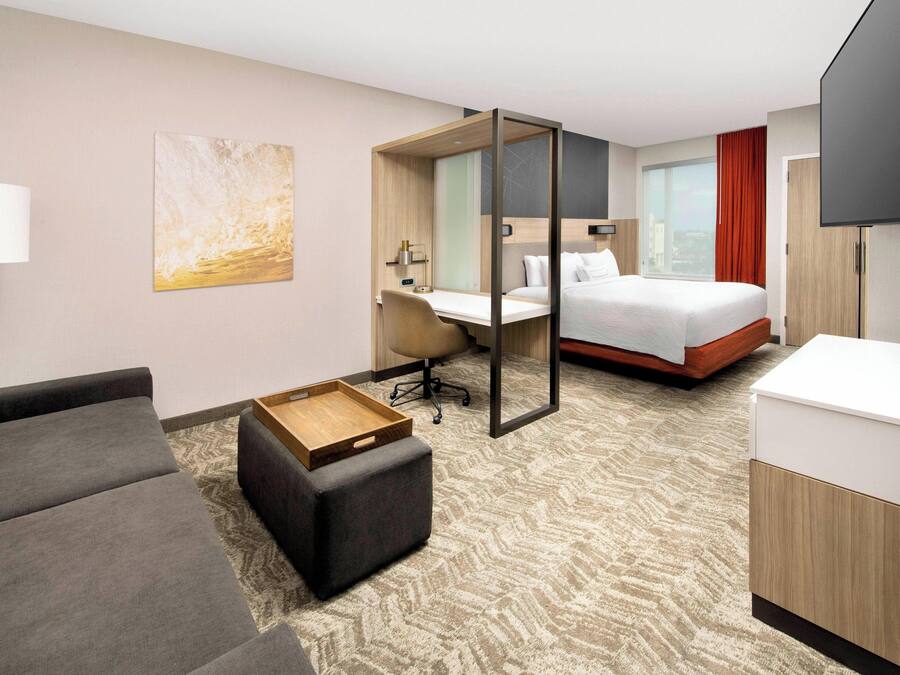 A hotel room with a bed, a desk, a chair, a sofa, a TV, and a lamp.
