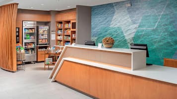 Zona de recepción de hotel con un mostrador de madera, un gran mural en la pared y varios aperitivos y bebidas en estantes.