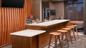 A modern bar area with a long counter, wooden stools, and a television mounted on the wall. - SpringHill Suites by Marriott Punta Gorda Harborside (Punta Gorda)