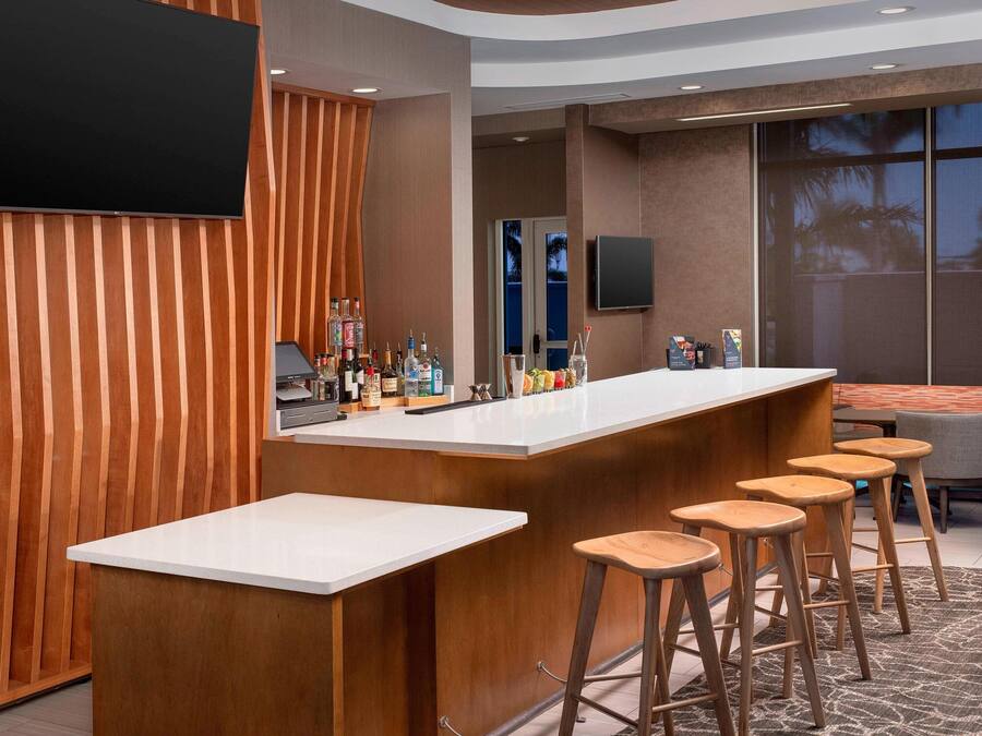 A modern bar area with a long counter, wooden stools, and a television mounted on the wall.