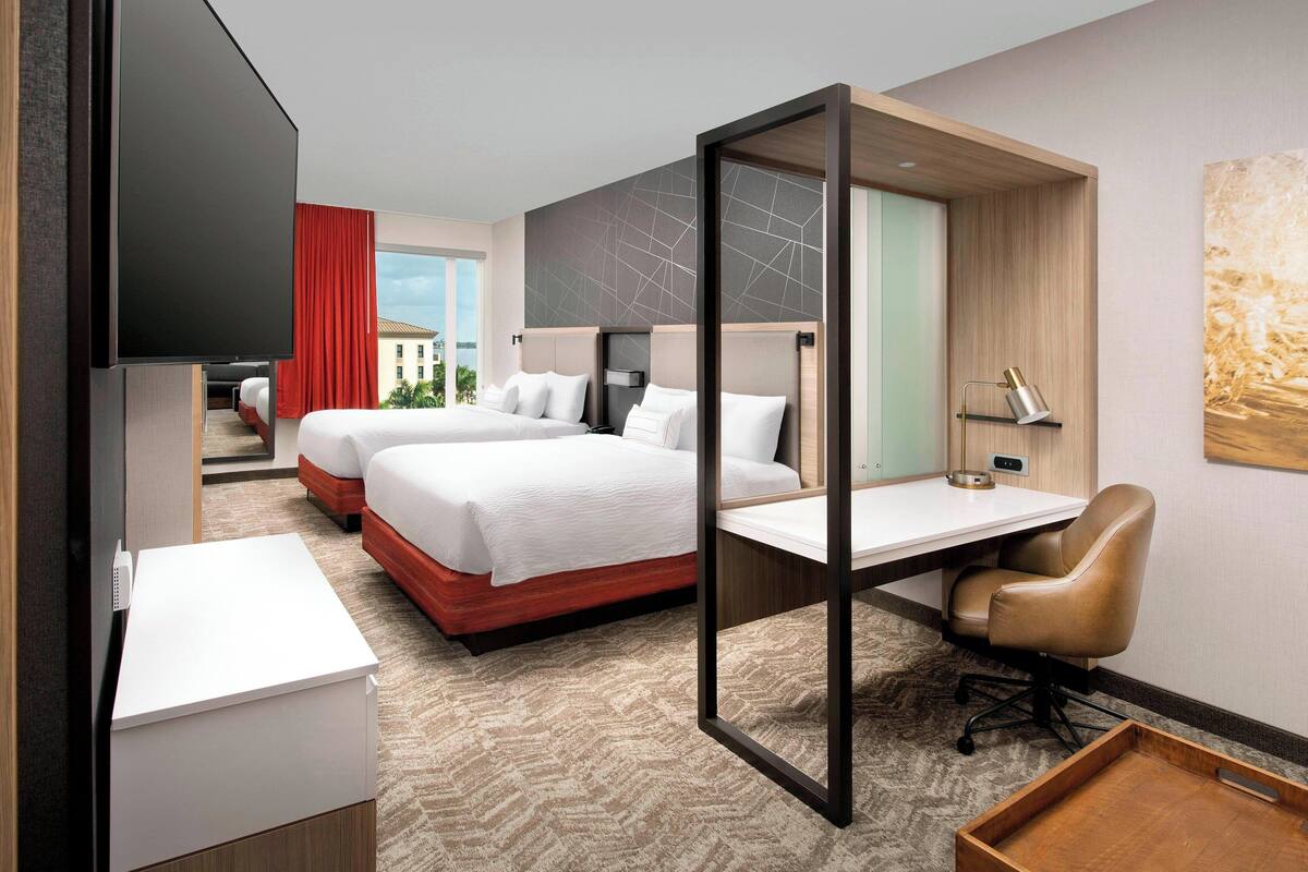 A hotel room with a bed, a desk, a chair, a TV, and a window with a view.
