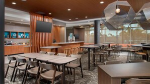 A modern restaurant with multiple dining tables and chairs, a bar area, and a large window providing a view of the outdoors. - SpringHill Suites by Marriott Punta Gorda Harborside (Punta Gorda)