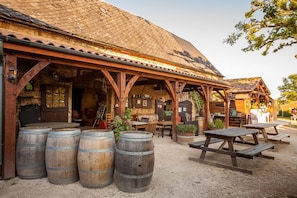 A rustic outdoor seating area with wooden tables and benches, surrounded by large wooden barrels. - Camping Domaine Des MATHEVIES (Sainte-Nathalene)