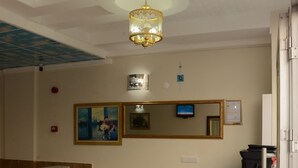 Una zona de recepción con mostrador de mármol, espejo con marco dorado y una columna decorativa.