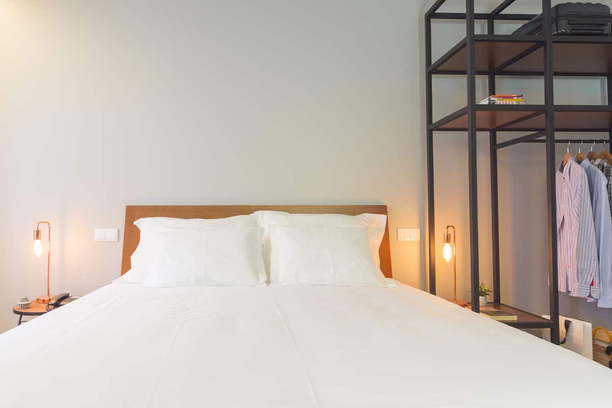A neatly made bed with white linens, a wooden headboard, and two bedside lamps.