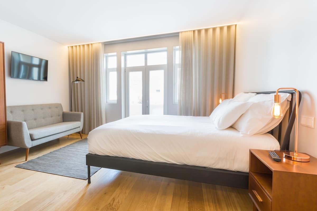 A modern hotel room with a bed, a sofa, a desk, and a wardrobe.