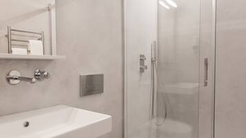 Un baño moderno con ducha de vidrio, un lavamanos blanco y un perchero para toallas.