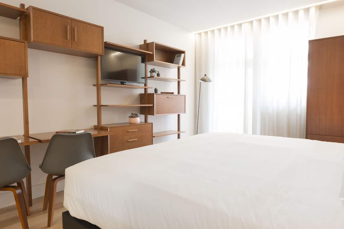 A hotel room with a bed, a desk with a chair, a TV, wooden cabinets, and a wardrobe.