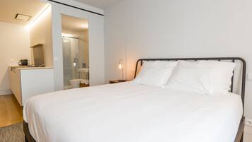 Et moderne hotelværelse med en stor seng, et natbord med lampe, et lille skrivebord og et bruseområde.