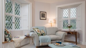 A cozy living room with a light blue sofa, a wooden side table with a vase, and a red patterned rug. - East Gatehouse Lodge (Crieff)