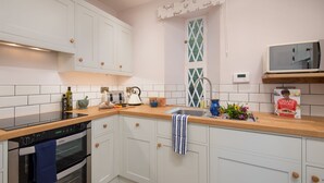 A kitchen with white cabinets, a wooden countertop, a stove, a sink, and a microwave. - East Gatehouse Lodge (Crieff)