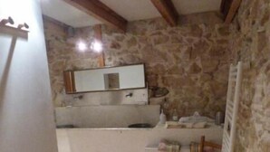A compact kitchen with a stone wall, a built-in sink, and a chair.