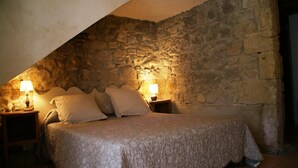 A bedroom with a stone wall, a bed with a patterned bedspread, two bedside lamps, and a nightstand.