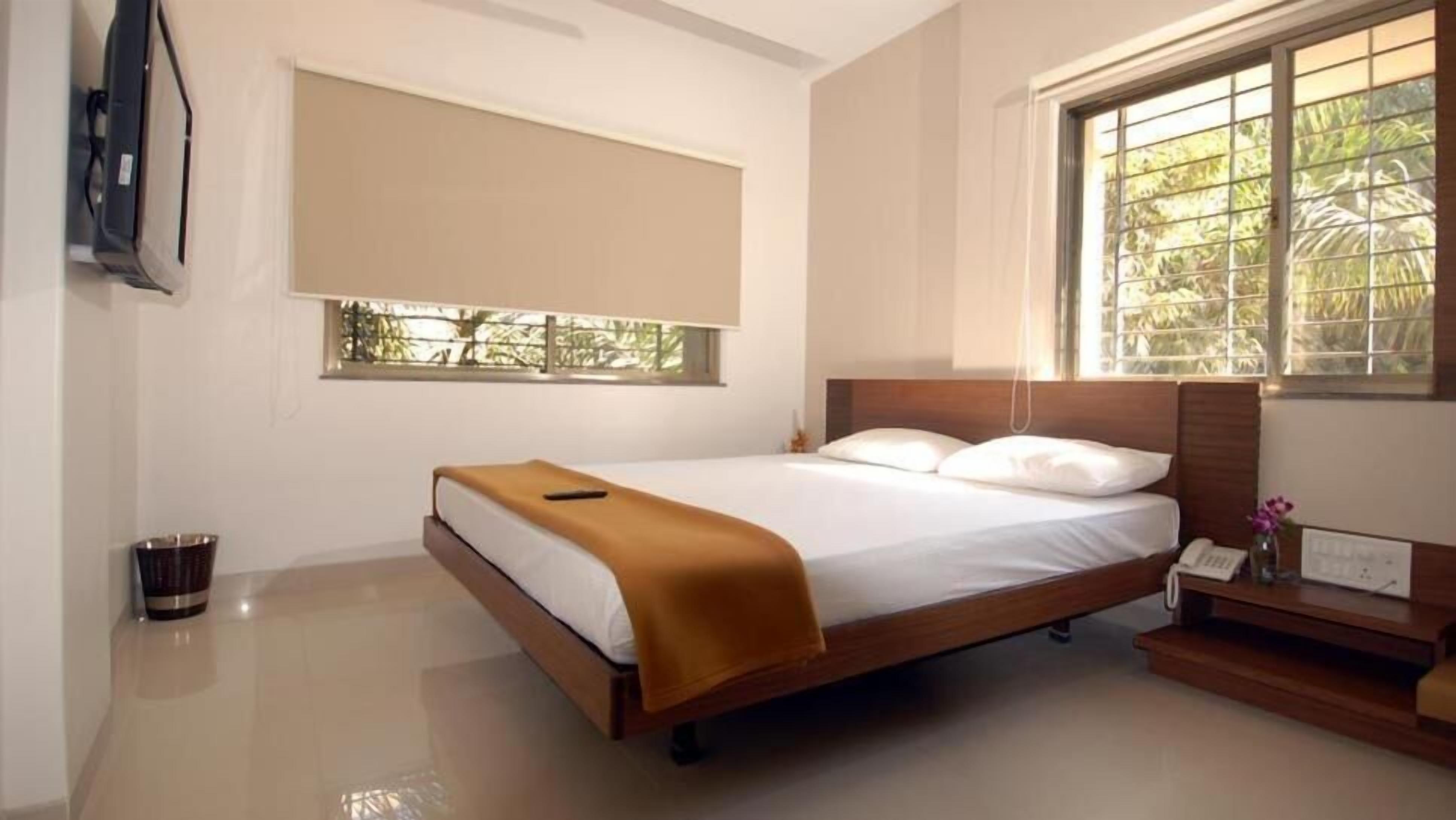 Une chambre à coucher avec un lit, une table de chevet avec un téléphone, une fenêtre donnant sur un paysage verdoyant et un téléviseur fixé au mur.