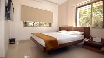 A bedroom with a bed, a bedside table with a phone, a window with a view of greenery, and a wall-mounted TV.