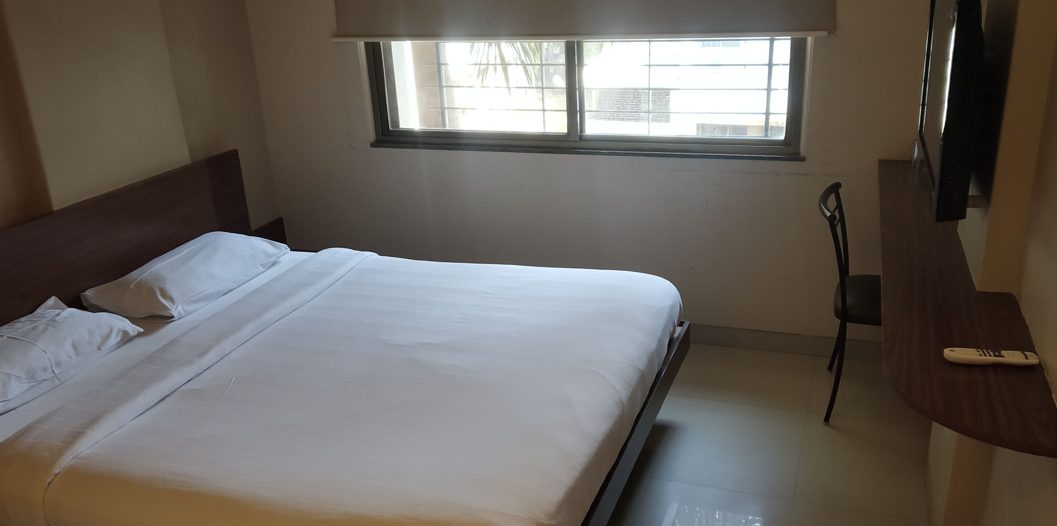 Een hotelkamer met een bed, een raam, een televisie en een bureau.