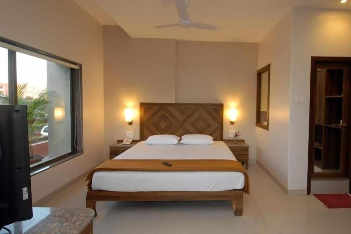 A hotel room with a bed, bedside lamps, a ceiling fan, a large window, and a wardrobe.