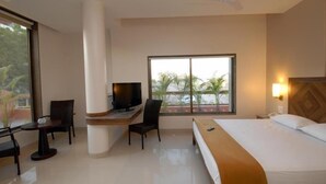 Habitación de hotel con cama, escritorio con televisor, una silla y ventana con vista a palmeras y coches aparcados.
