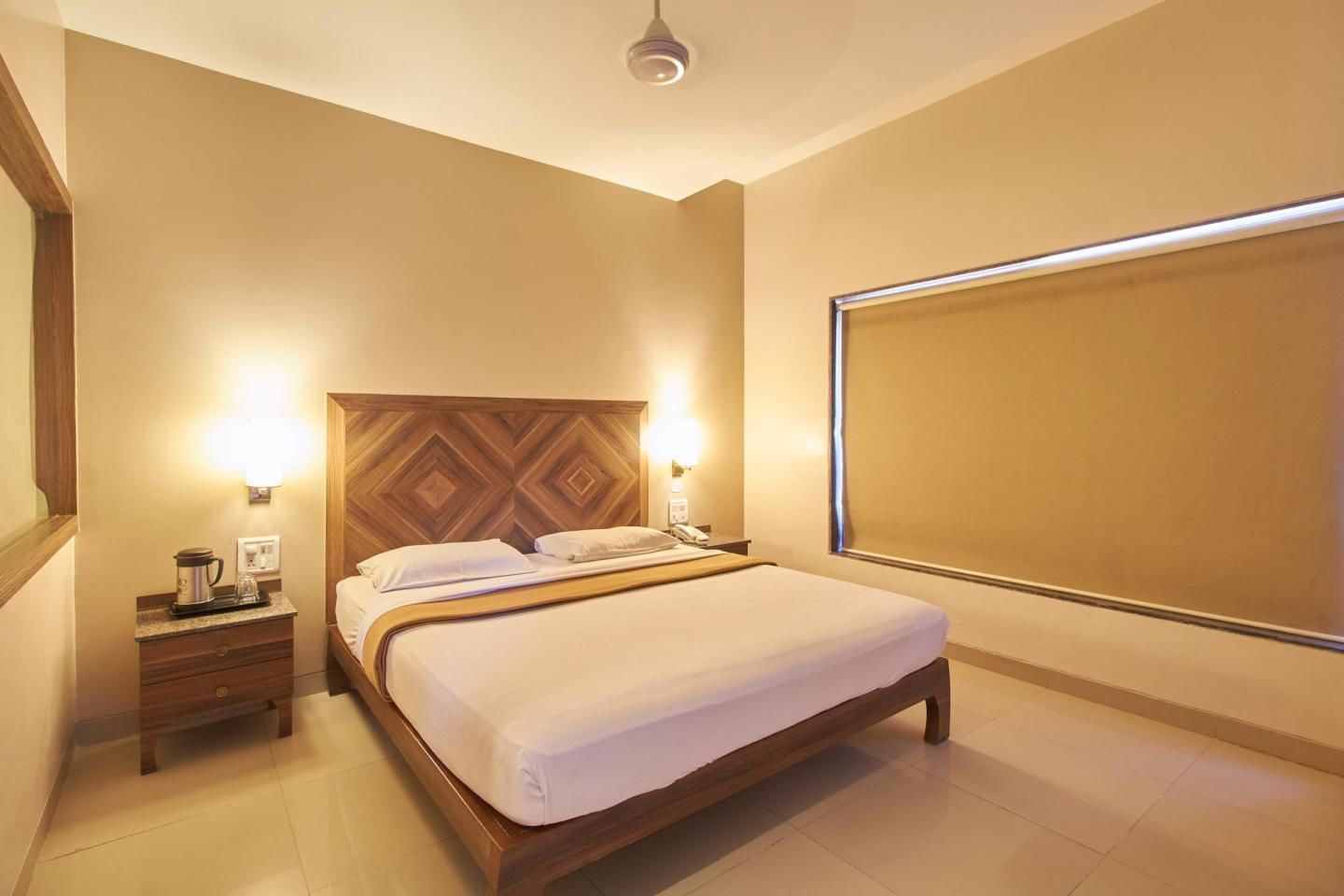 A hotel room with a wooden headboard, a bed with white linens, a nightstand with a lamp, and a large window.