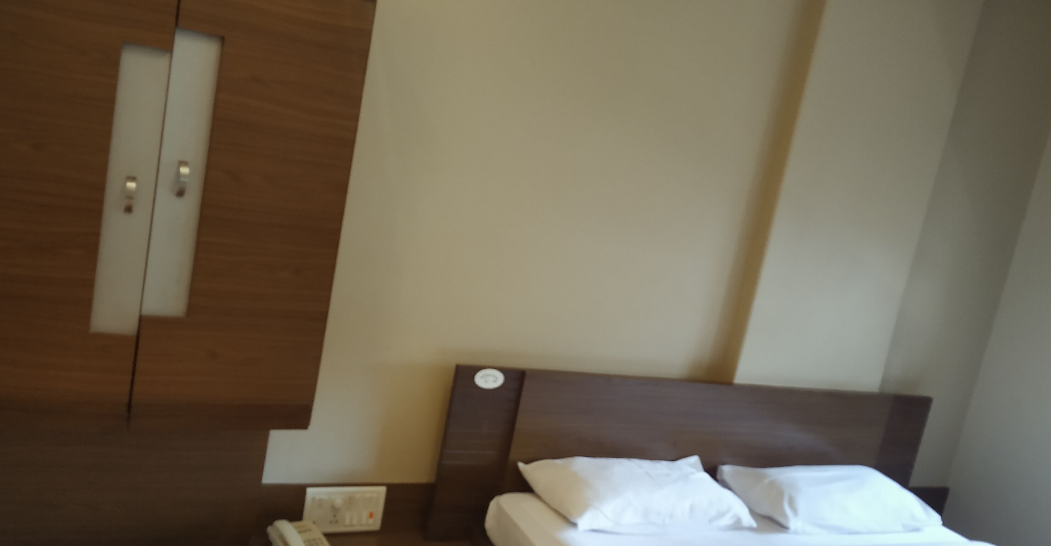 A bedroom with a wooden wardrobe, a bedside table with a phone, and a bed with white bedding.