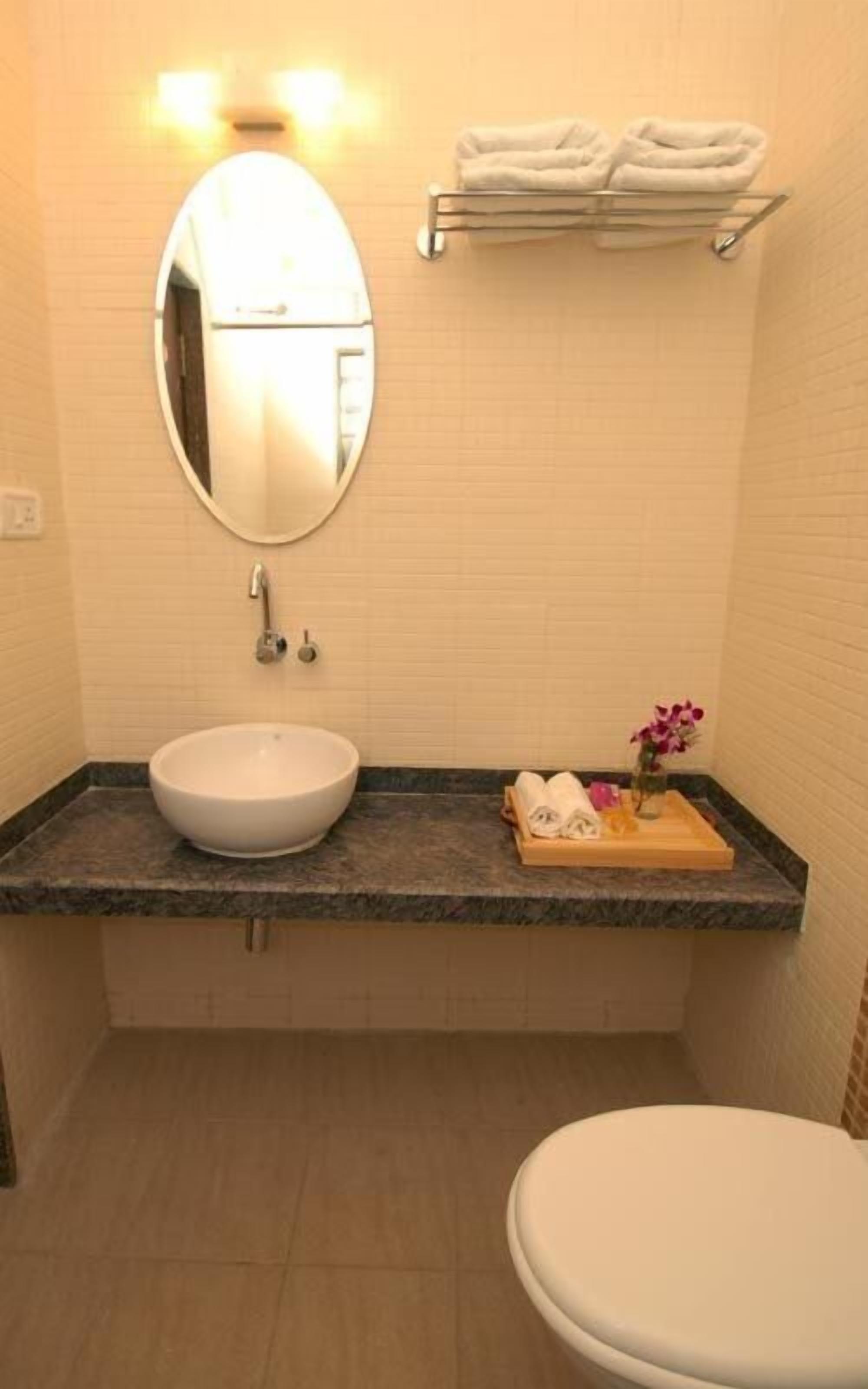 Un baño con un espejo redondo, un lavabo blanco, un inodoro y un perchero con toallas dobladas.