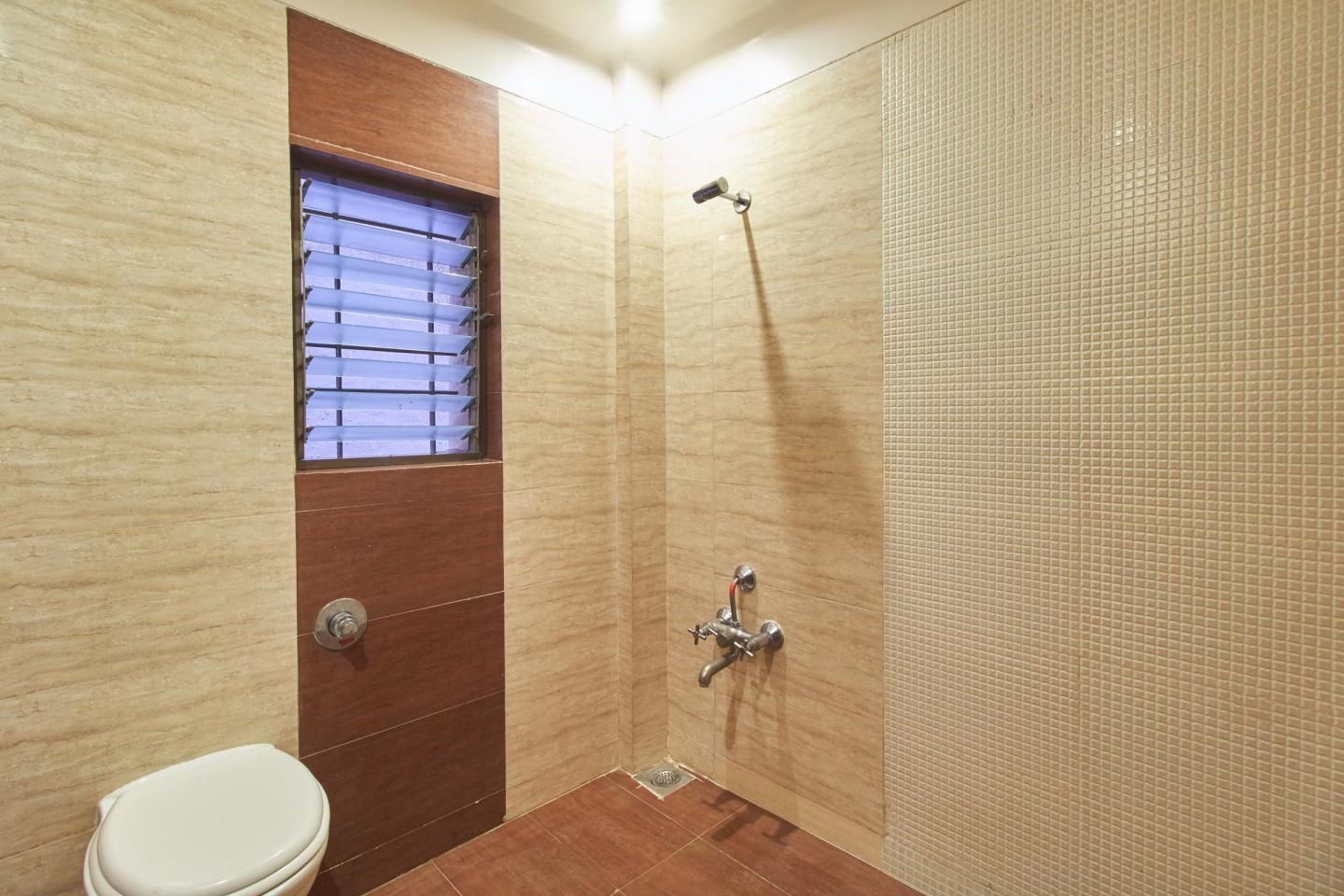 A small bathroom with a toilet, a shower, and a window with blinds.